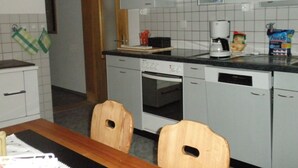 Keittiössä on valkoiset kaapit, kahvinkeitin, astianpesukone ja ruokapöytä tuoleineen.