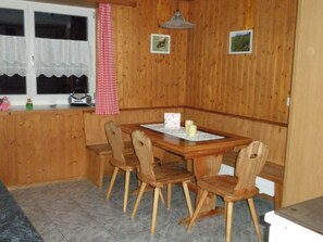 A wooden interior with a dining table and chairs, a window with curtains, and a checkered cloth hanging. - Casa Curgnun Collenberg, Morissen, (Morissen), 43002B by Interhome (Morissen)