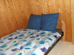 A bed with a floral-patterned bedspread and two pillows, set against a wooden wall. - Casa Curgnun Collenberg, Morissen, (Morissen), 43002B by Interhome (Morissen)