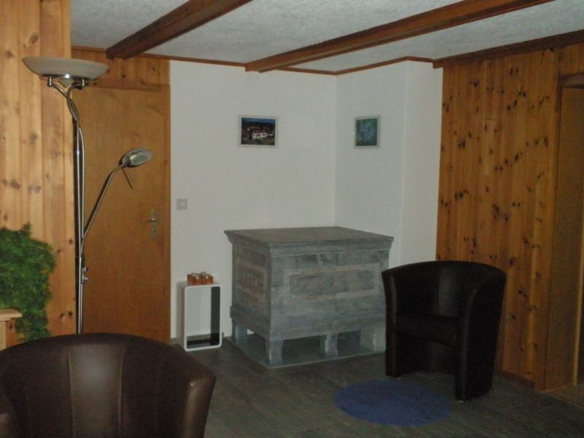 Ein Zimmer mit Holzwänden, einem weißen Schrank, einem schwarzen Stuhl, einer Stehlampe und einer kleinen Pflanze.