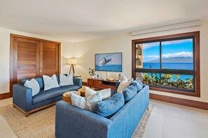 Ein Wohnzimmer mit zwei Sofas, einem Fernseher und einem großen Fenster mit Meerblick.