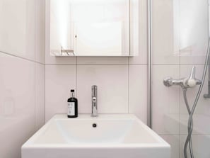 Ein Badezimmer mit einem weißen Waschbecken, einem Spiegel, einer Handbrause und einer Flasche Handseife.