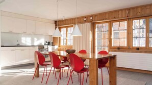 A modern kitchen with white cabinets, a wooden dining table, red chairs, and pendant lights. - Casa Fulin, Obersaxen Affeier, (Obersaxen Affeier), 34075B by Interhome (Obersaxen Affeier)