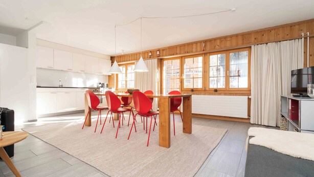 A modern kitchen with white cabinets, a dining area with red chairs, and a TV on the right. - Casa Fulin, Obersaxen Affeier, (Obersaxen Affeier), 34075B by Interhome (Obersaxen Affeier)