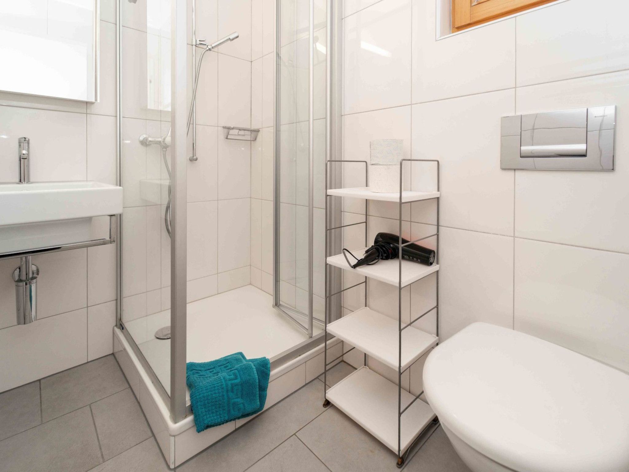 Een moderne badkamer met een douchecabine van glas, een wit wastafeltje en een toilet.