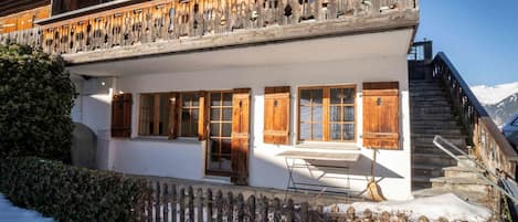 Un chalet en bois à deux étages, doté d’un balcon, de grandes fenêtres et d’un escalier menant à un point de vue sur la montagne.