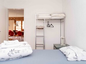 Habitació d'hotel amb dos llits, un armari, una taula de treball i una zona de menjador visible per una porta oberta.