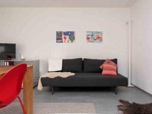 Ein modernes Wohnzimmer mit einer Couch, einem roten Sessel, einem Couchtisch und zwei Bildern an der Wand.