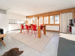 A modern kitchen with white cabinets, a dining area with a wooden table and red chairs, and a large window with curtains. - Casa Fulin, Obersaxen Affeier, (Obersaxen Affeier), 34075B by Interhome (Obersaxen Affeier)