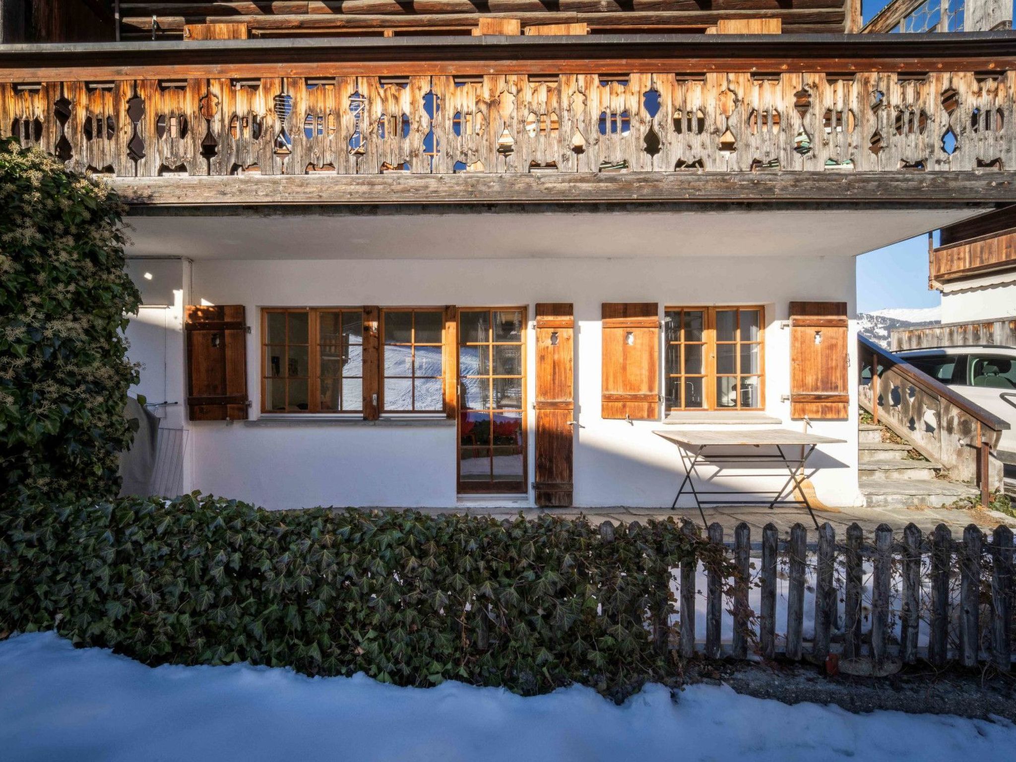 A two-story chalet with a wooden balcony, large windows, and a snow-covered ground.