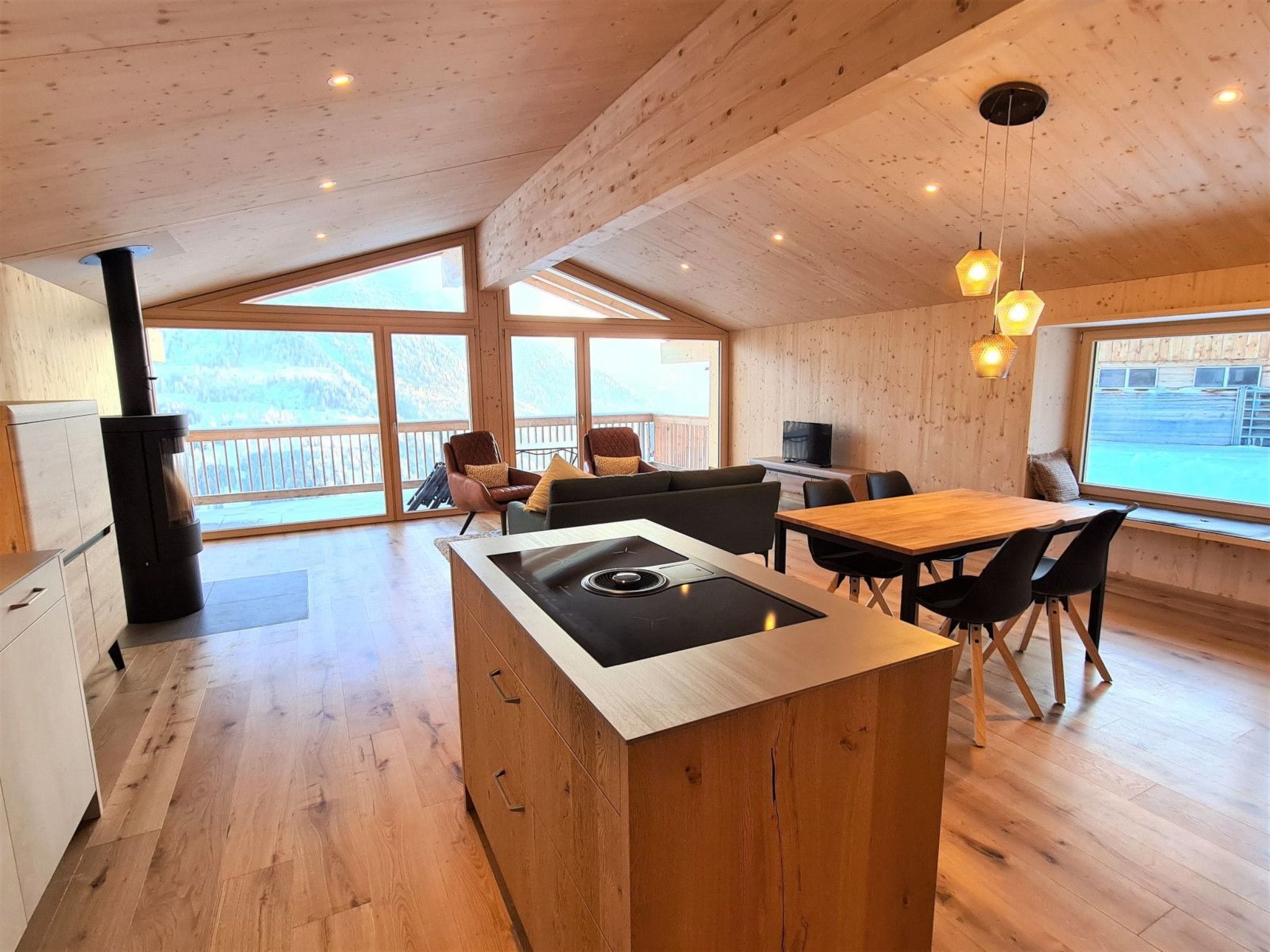 Una cocina moderna con una isla central, suelo de madera y amplios ventanales que ofrecen vistas al exterior.