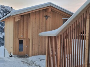 Ein Holzgebäude mit geneigtem Dach, einer Tür und einer Treppe, die zu einer Veranda führt.