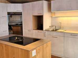 A modern kitchen with a central island, built-in oven, and a stainless steel sink.