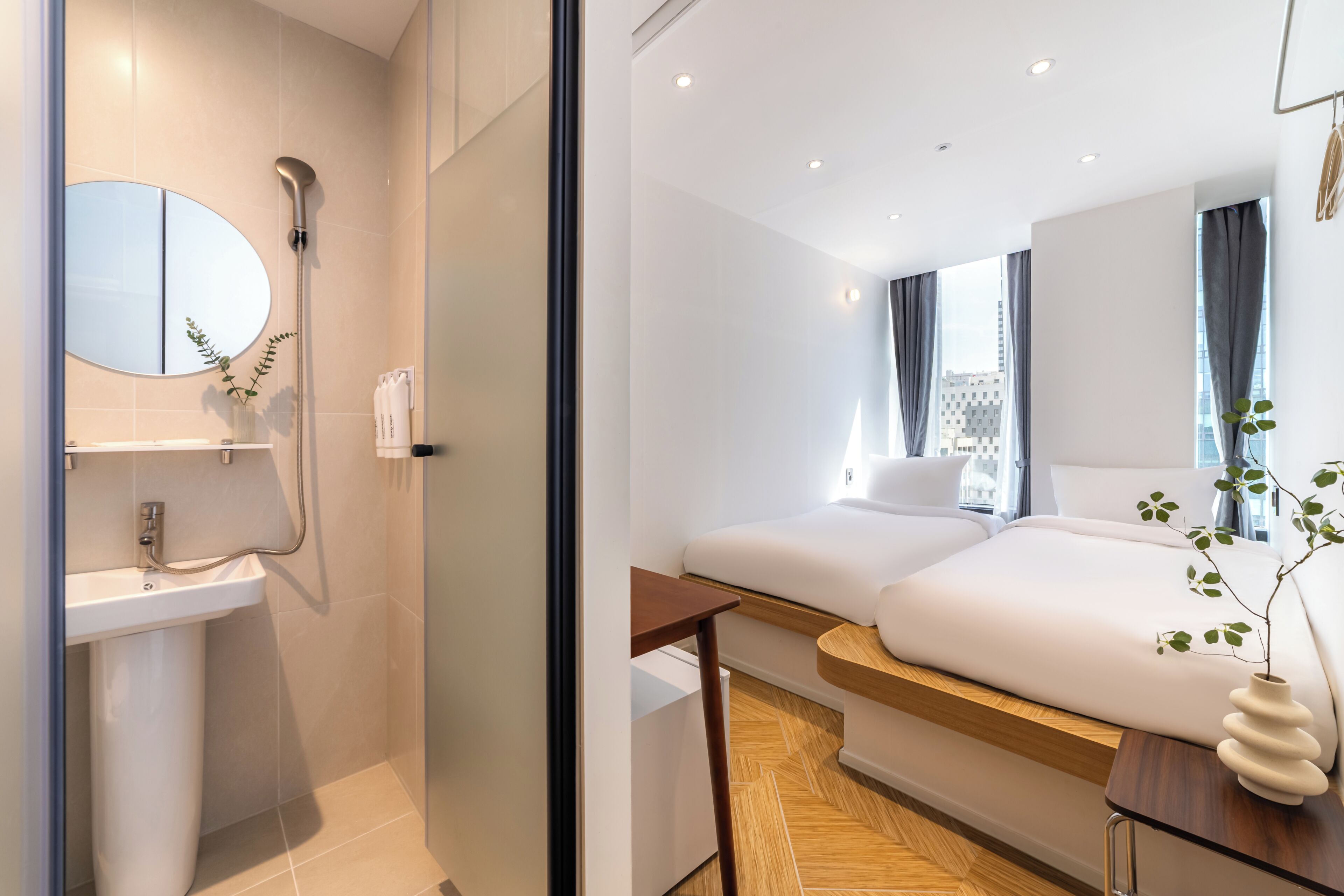 Una habitación de hotel moderna con baño, una cama, una mesita de noche y vistas a la ciudad.