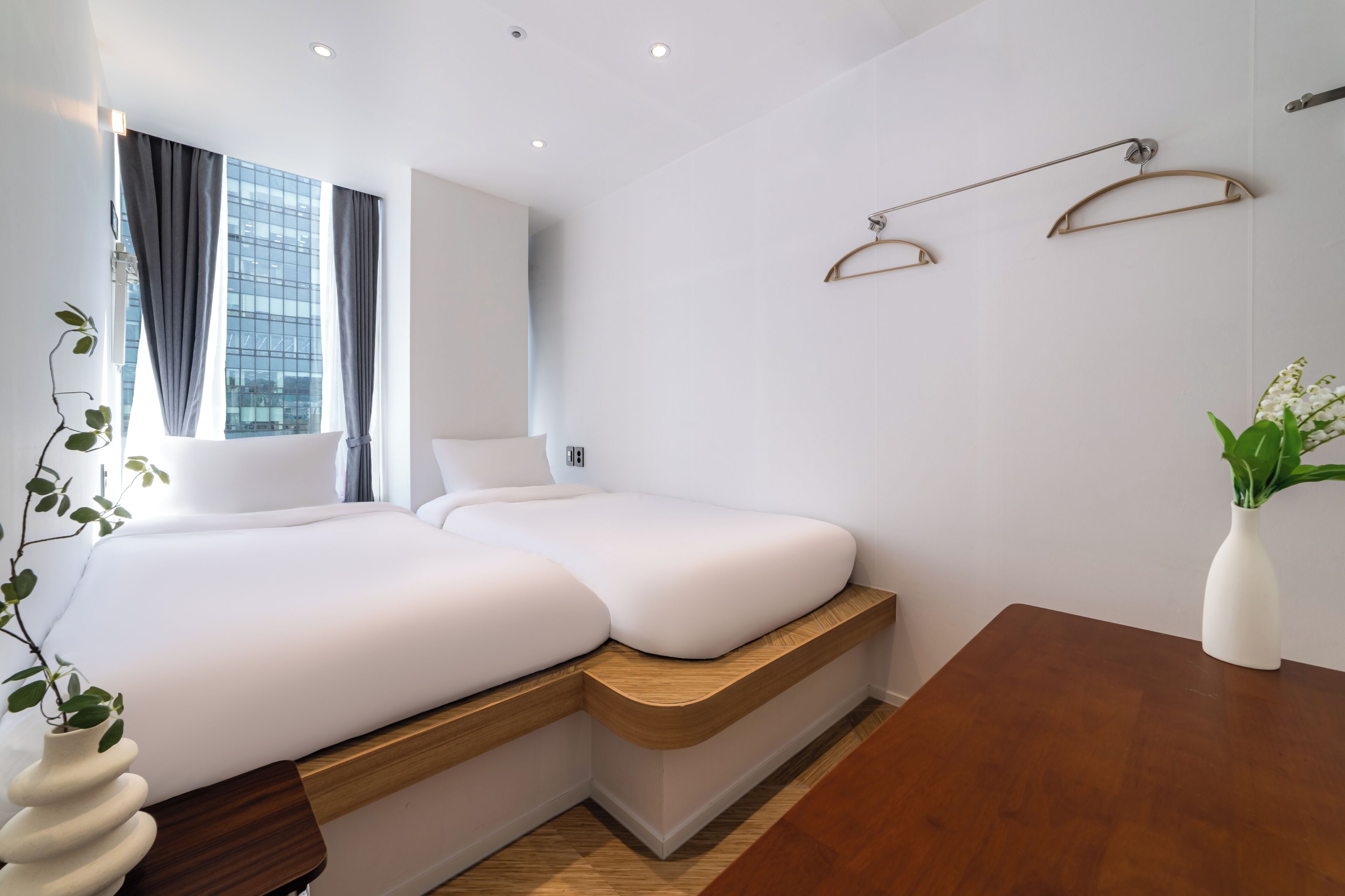 Une chambre d’hôtel moderne dotée d’un grand lit, d’une banquette intégrée, d’un plancher en bois et offrant une vue sur la ville grâce à de grandes fenêtres.