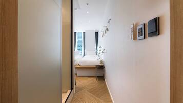 Una habitación de hotel moderna con suelo de madera, una cama con ropa de cama blanca, una mesita de noche y un panel de control en la pared.