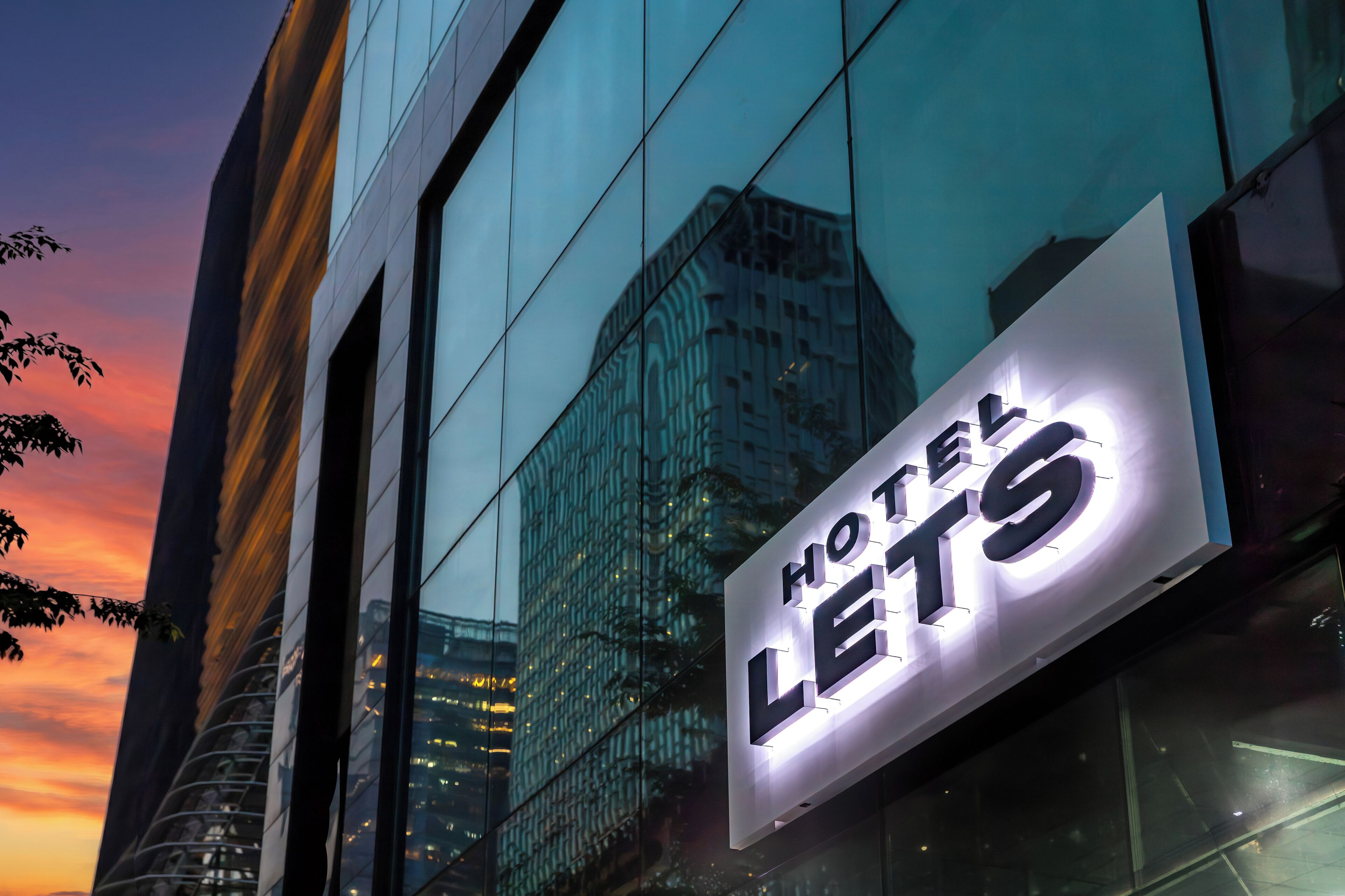 Señal de hotel con el nombre 'HOTEL LETS' sobre una fachada de edificio moderna.