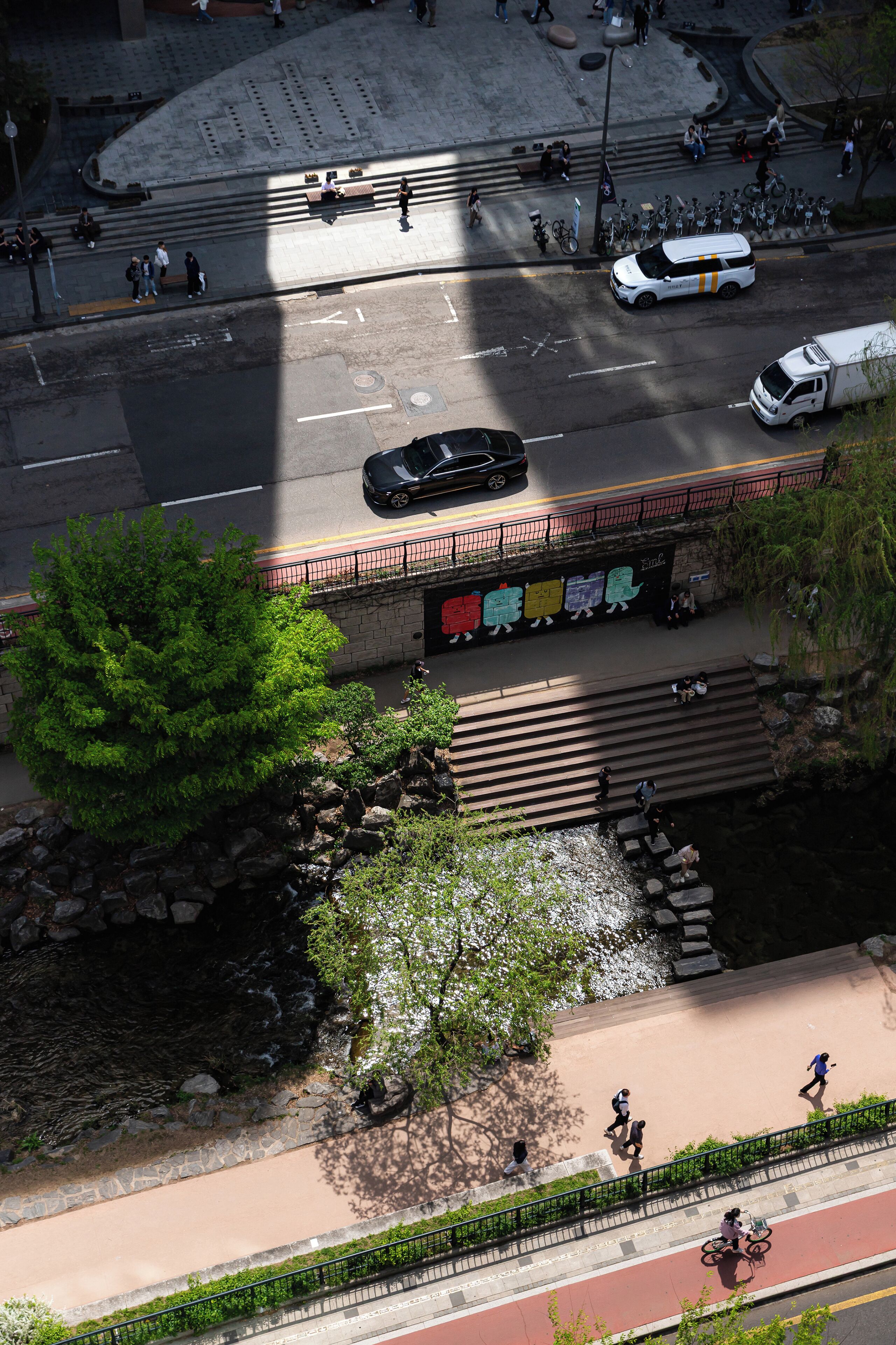 Une scène urbaine à plusieurs niveaux, avec un pont piétonnier, une piste cyclable et une rivière.