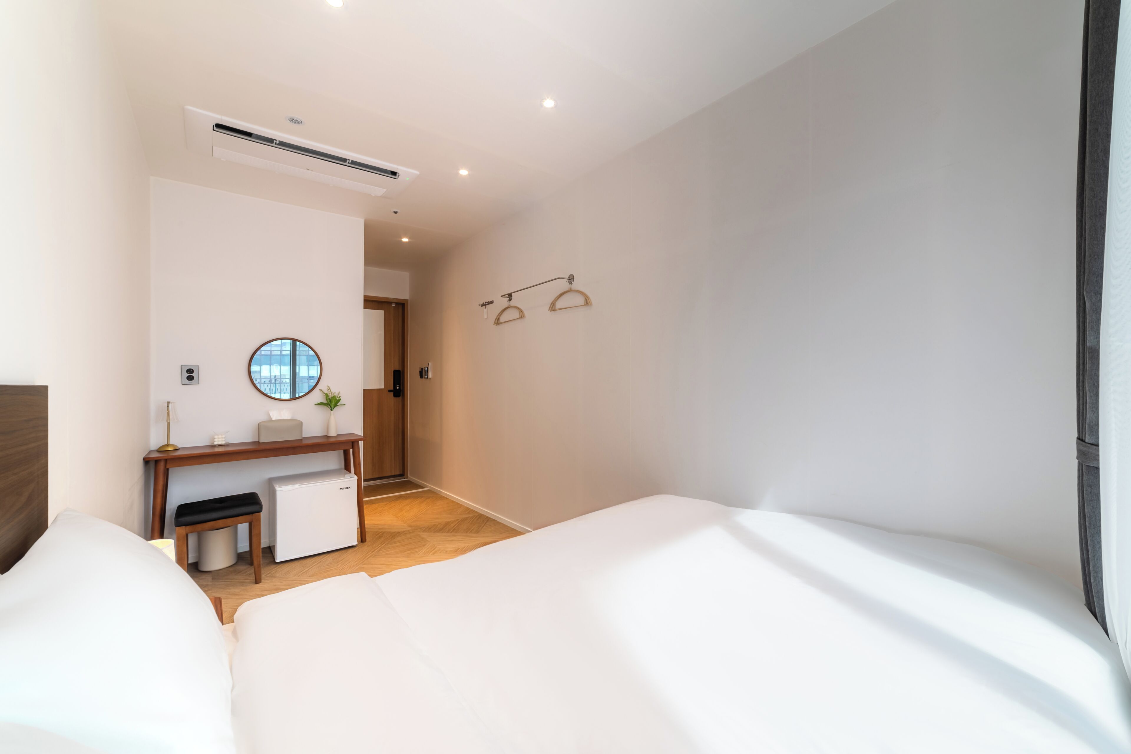 Habitación de hotel con cama, escritorio, refrigerador pequeño, espejo y puerta que da a otra habitación.