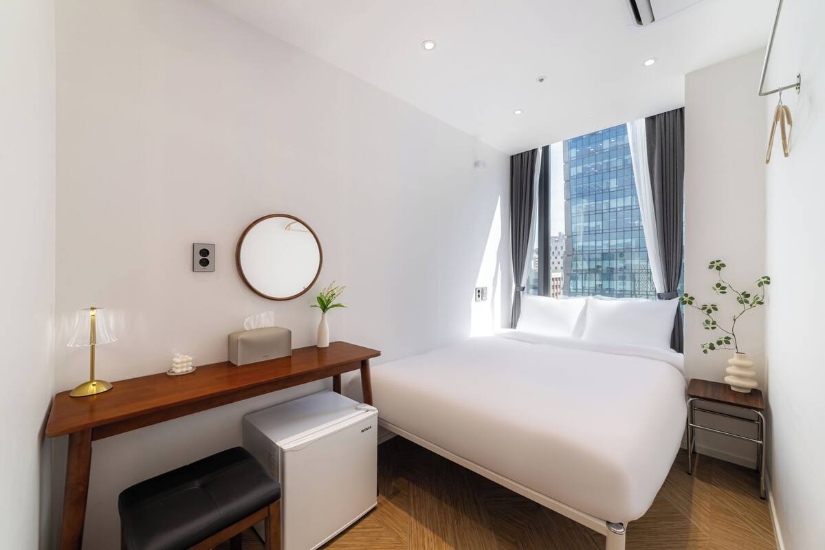 Una habitación de hotel moderna con cama, escritorio, silla y un refrigerador pequeño.