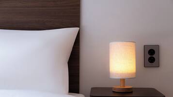 Una cama bien hecha con ropa de cama blanca, una mesita de noche con una lámpara y una lámpara de pared.