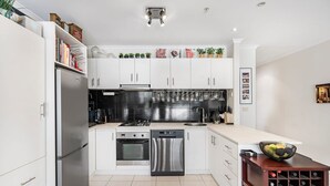 A modern kitchen with white cabinets, stainless steel appliances, and a wine rack. - Light-filled, spacious 2 bdrm Prahran apartment with free parking. (Prahran)