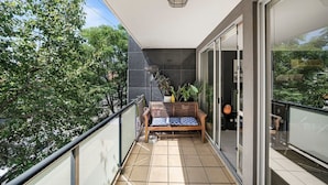 A balcony with a wooden bench, potted plants, and a view of trees. - Light-filled, spacious 2 bdrm Prahran apartment with free parking. (Prahran)
