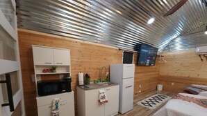 A compact room with a kitchenette, a bed, and a wooden wall.