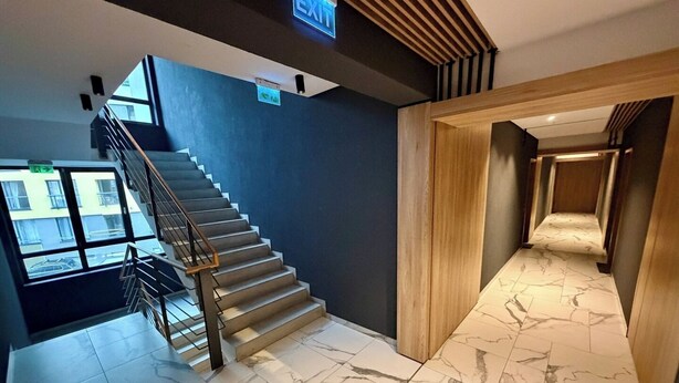 A modern staircase with a metal railing, a blue wall, and a wooden door leading to a hallway with marble flooring.