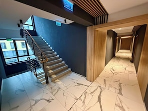 Un escalier moderne avec une rampe en métal, un mur bleu et une porte en bois donnant sur un couloir dont le sol est recouvert de marbre.