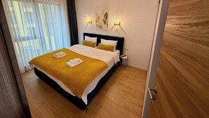 A hotel room with a bed, two bedside tables, a window with curtains, and a door.