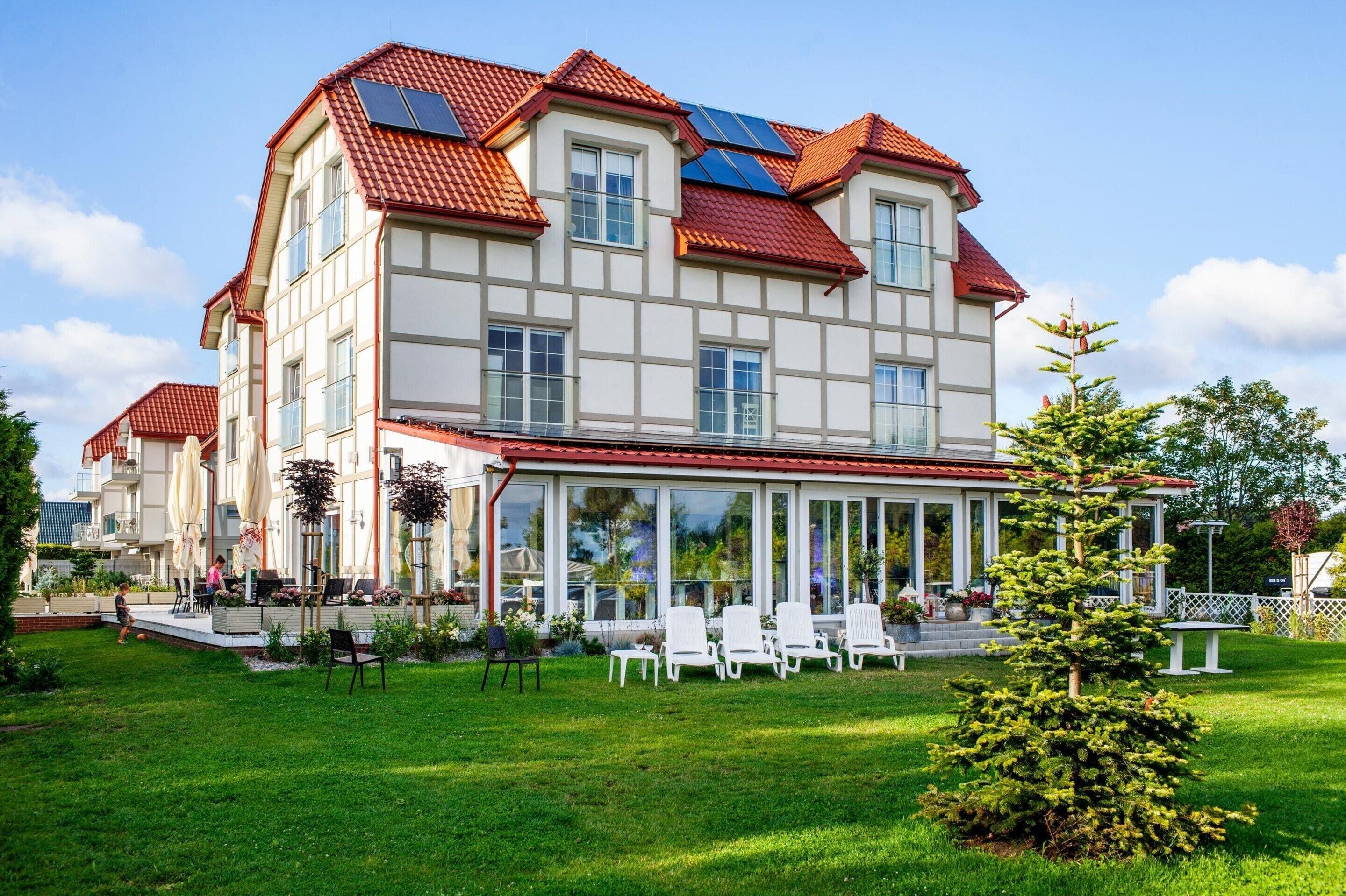 A large, multi-story building with a red-tiled roof, large windows, and a covered patio area with outdoor seating.