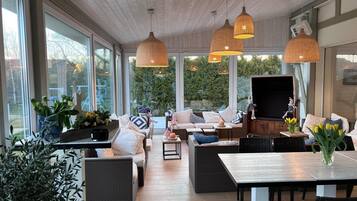 A spacious indoor area with large windows, wicker furniture, and hanging pendant lights.