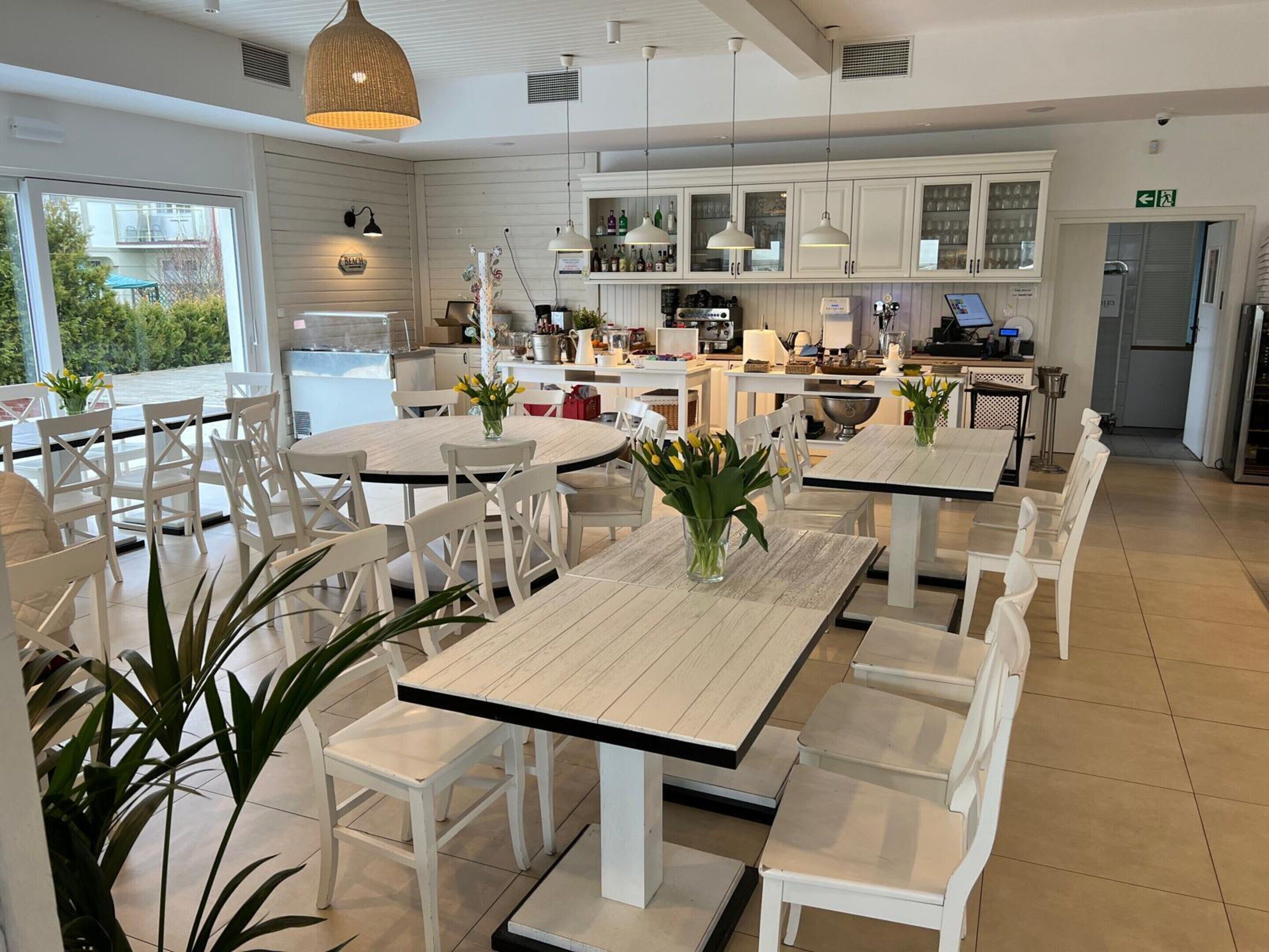 A modern kitchen with white cabinets, a dining area with white tables and chairs, and a view of the outdoors.