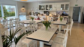 A modern kitchen with white cabinets, a dining area with white tables and chairs, and a view of the outdoors.