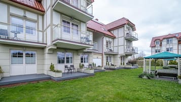 Um edifício residencial com vários andares, varandas, área de estar coberta ao ar livre e um gramado bem cuidado.