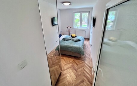 A narrow hallway leading to a bedroom with a bed, a window, and a radiator.