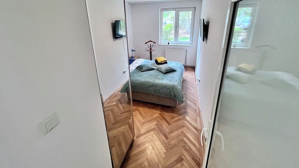 A narrow hallway leading to a bedroom with a bed, a window, and a radiator.
