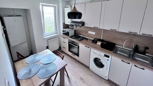 A compact kitchen with a built-in oven, microwave, and washing machine, a dining table with placemats, and a window providing natural light.