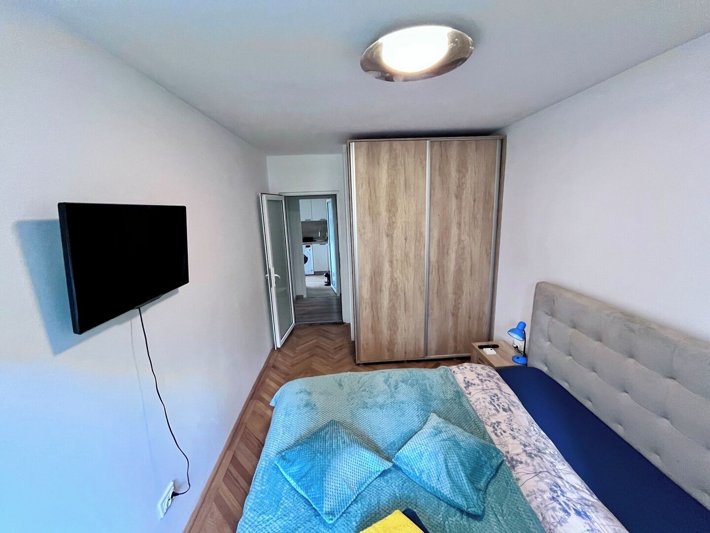 Une chambre à coucher comprenant un lit, un téléviseur fixé au mur, une armoire et une porte donnant sur une salle de bain.