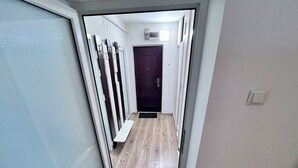 A narrow hallway with a wooden floor, a dark door at the end, and a coat rack on the left.