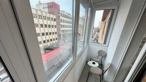 Un balcon étroit donnant sur une rue de la ville, une petite table ronde et deux chaises.