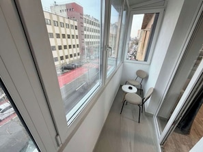Un balcon étroit donnant sur une rue de la ville, une petite table ronde et deux chaises.