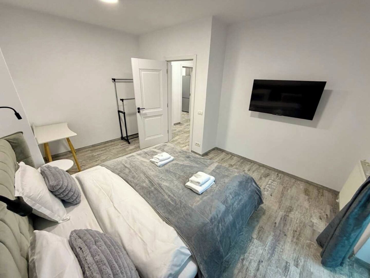 Un dormitorio moderno con cama, televisor, puerta y una mesita.