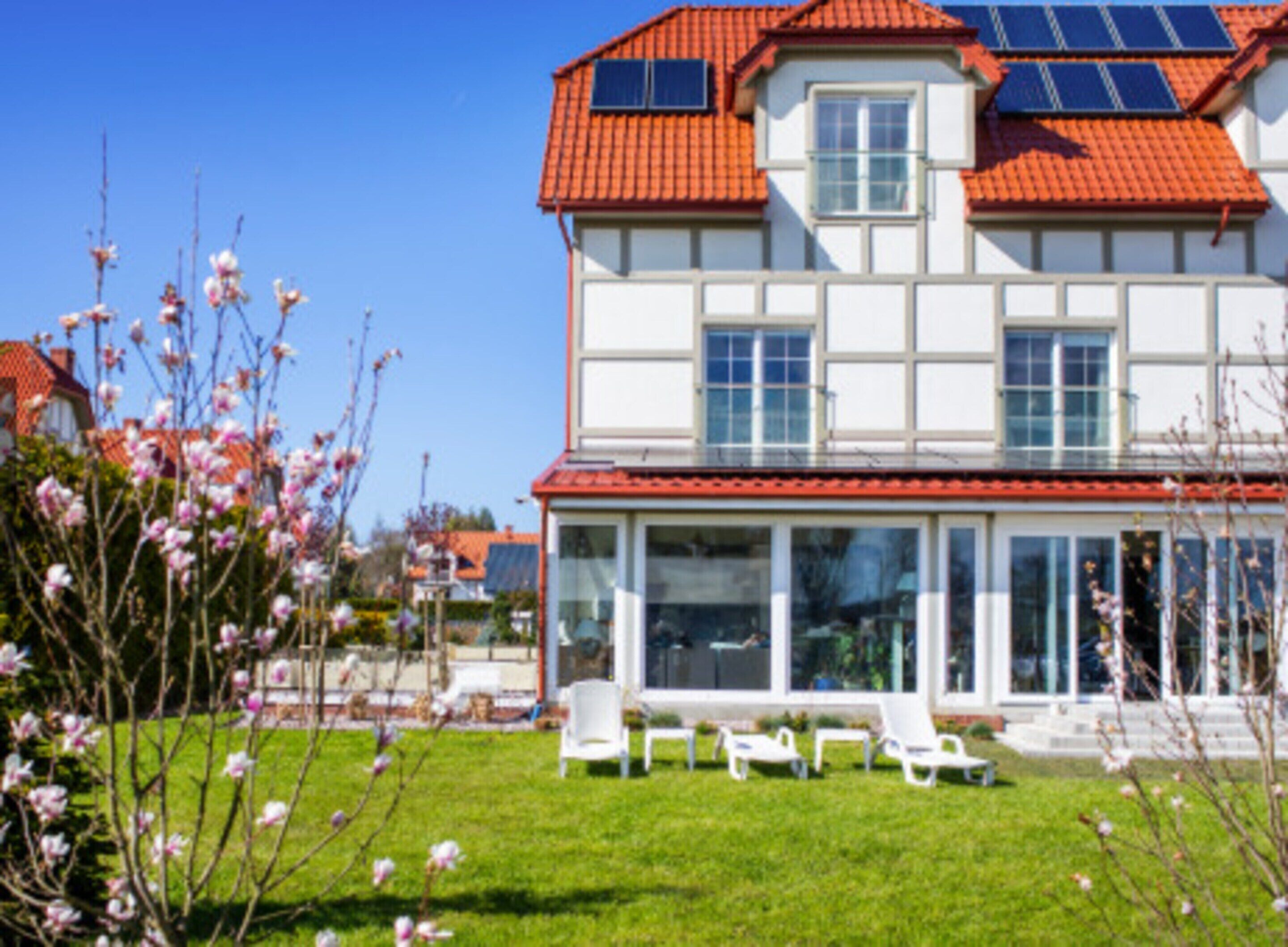 A two-story house with a red-tiled roof, large windows, and a covered patio area with white chairs.