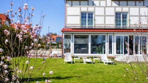 A two-story house with a red-tiled roof, large windows, and a covered patio area with white chairs. - Comfortable Apartment With a Balcony (Krokowa)