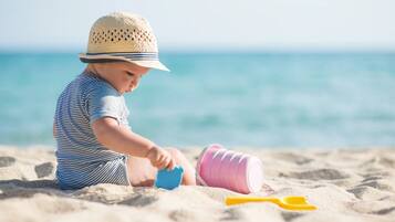 A child playing with toys on a sandy beach with the ocean in the background.