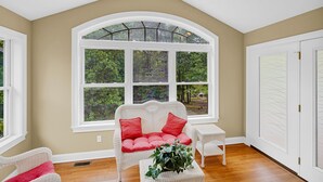 A room with a large arched window, a white sofa with red cushions, a small white table, and a potted plant. - Lakefront Retreat with private dock, game room, bar, and sunroom views (Cadiz)