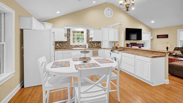 A kitchen with white cabinets, a dining table with chairs, a chandelier, and a television. - Lakefront Retreat with private dock, game room, bar, and sunroom views (Cadiz)