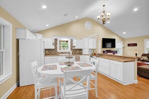 A kitchen with white cabinets, a dining table with chairs, a chandelier, and a television.
